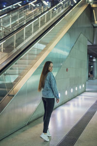 Full length portrait of woman standing by illuminated wall