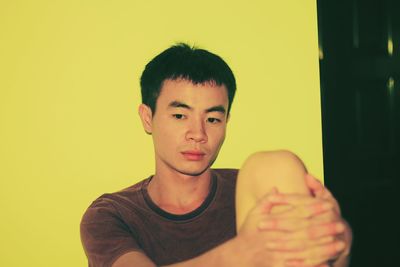 Young man sitting against yellow wall
