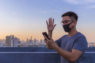 Asian man wearing face mask to protect from virus and make a video call with smartphone.