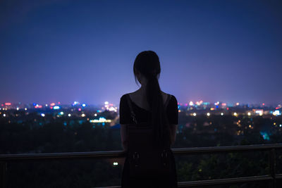 Rear view of woman standing against illuminated city at night