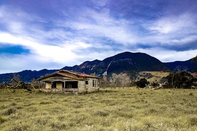 House on field by mountains against sky
