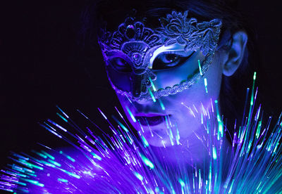 Portrait of woman wearing venetian mask with fiber optic against black background