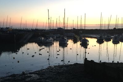 Boats moored at harbor against sky during sunset