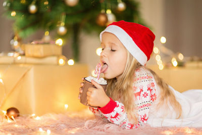 Cute girl holding hot chocolate while lying down on floor at home