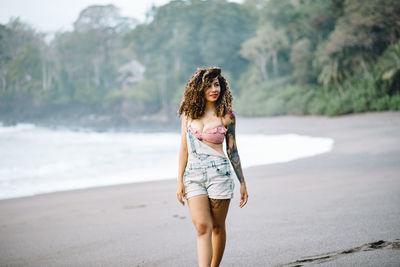 Seductive woman with curly hair standing at beach