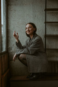 Young woman looking away while standing against wall