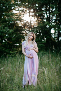 Happy pregnant woman standing on field