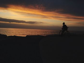 Silhouette man sitting on bicycle by sea against sky during sunset