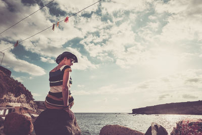 Woman standing on rock by sea against sky