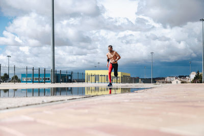 Shirtless man running by puddle on street against cloudy sky