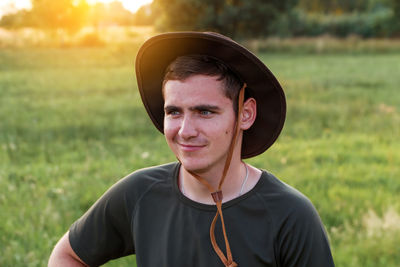 Young man smiling farmer in cowboy hat at agricultural field on sunset with sun flare. closeup 