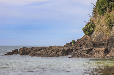 Man walking on cliff at beach against sky