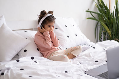 Cute girl listening music while sitting on bed