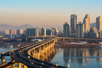 Bridge over river by buildings in city against sky