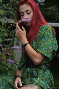 Young woman with red hair and a long green dress, smelling a lilly flower 