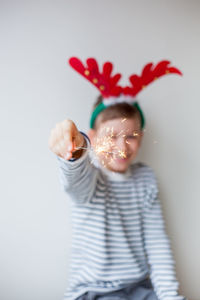 Happy boy holding sparkler while standing by wall