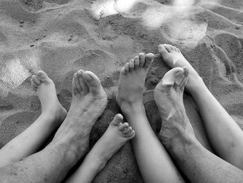 Low section of people with barefoot resting on sand at beach