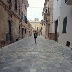 Rear view of man walking on road along buildings