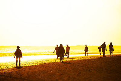 Silhouette of people walking on beach at sunset