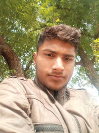 Portrait of young man standing against trees