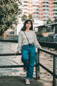 Portrait of young woman standing against railing