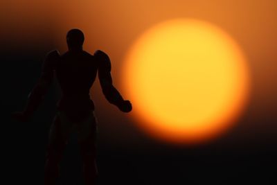 Rear view of silhouette man standing against orange sky