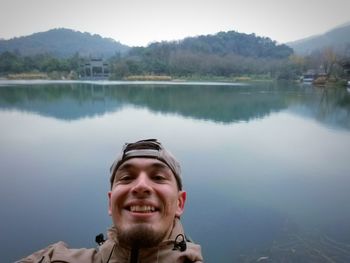 Portrait of smiling young man by lake against mountains