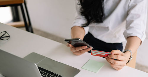 Midsection of woman using mobile phone on table