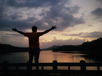 Rear view of man standing on bridge against sky during dusk