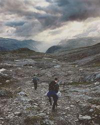 Rear view of hikers walking on mountain against cloudy sky