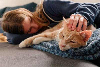 A young adolescent girl lying on a couch finds comfort by snuggling and petting her tabby cat