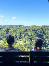 Rear view of couple sitting on mountain against sky