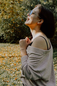 Side view of young woman standing against trees