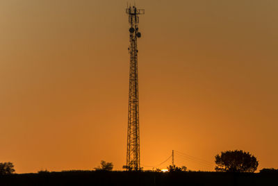 Low angle view of silhouette communications tower against sky during sunset