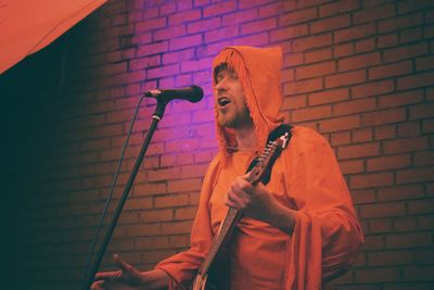 Young man singing against brick wall