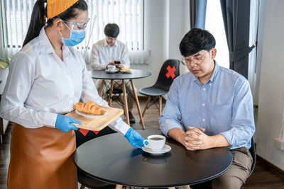 Female barista serving coffee to customer at cafe during pandemic