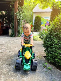 A toddler boy is playing with a toy tractor outdoors. a little cute boy of one and a half years