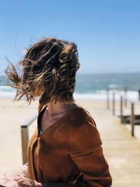 Rear view of woman at beach against sky on a windy day