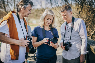 Senior male and female friends using cameras while standing at park