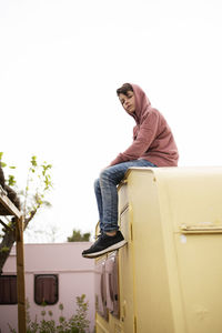 Low view of a young boy sitting on the top of a caravan