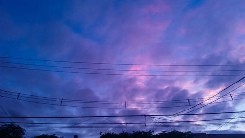 Low angle view of electricity pylon against cloudy sky