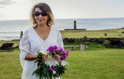 Woman with flowers standing on field against sea