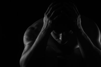 Shirtless sad man with head in hands against black background