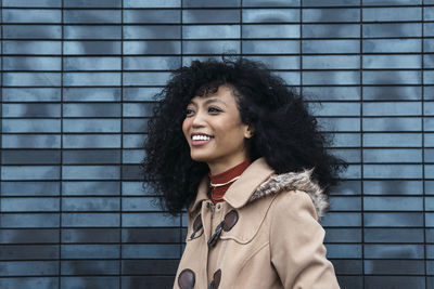 Happy young woman with curly hair in front of blue wall