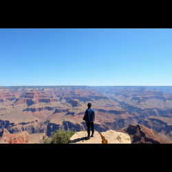 Man standing on landscape against clear blue sky