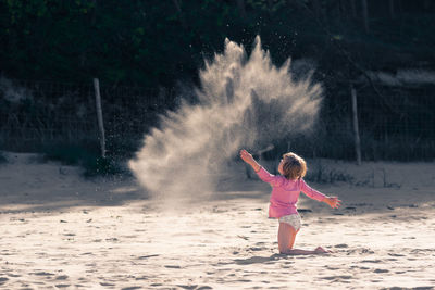 Girl throwing sand at beach on sunny day