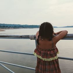 Rear view of girl standing by railing against sea