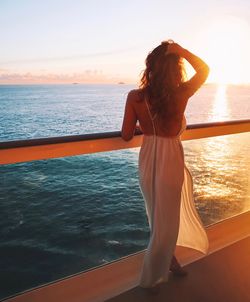 Woman standing by sea against sky during sunset