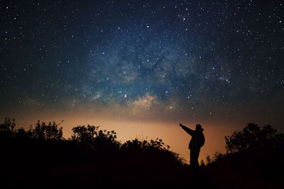 Silhouette person pointing against sky at night