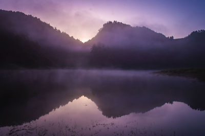 Scenic view of lake by mountains against sky during sunset